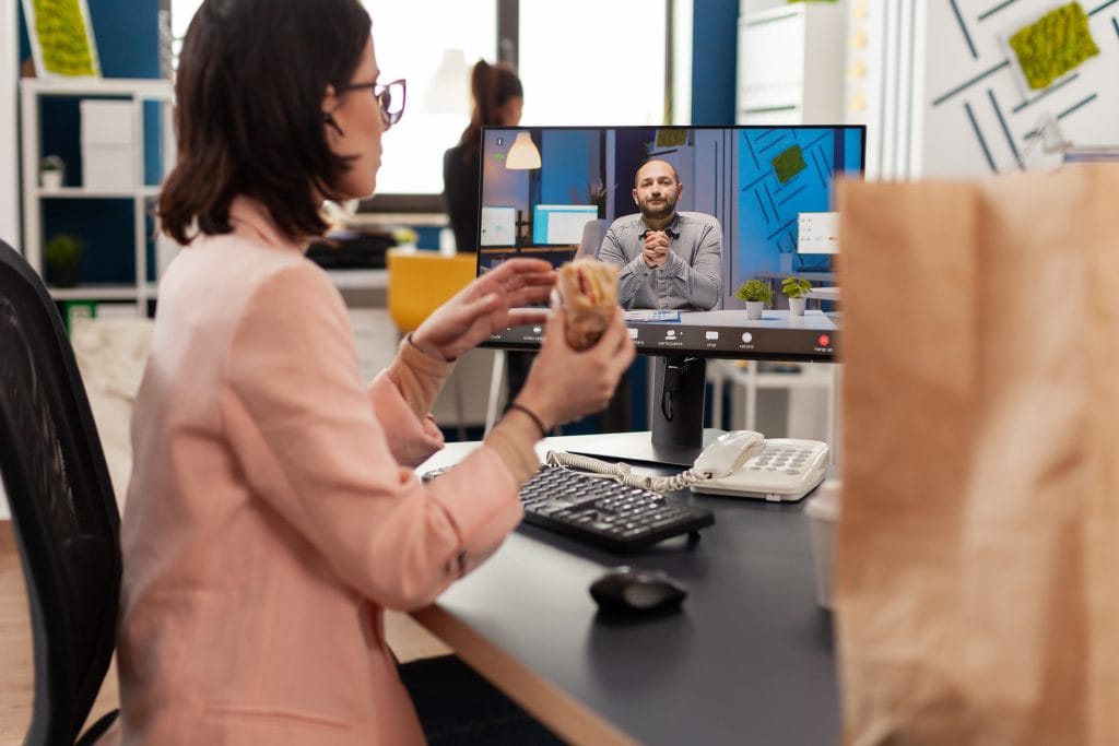 Businesswoman eating delivery takeaway sandwich during online videocall conference